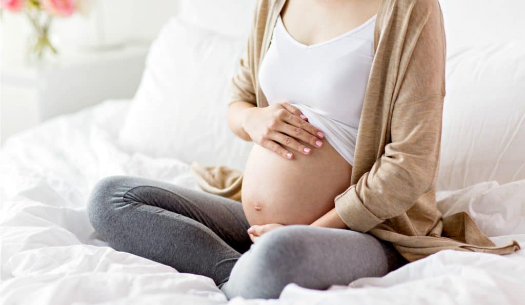 pregnant woman sitting on bed considering a home birth