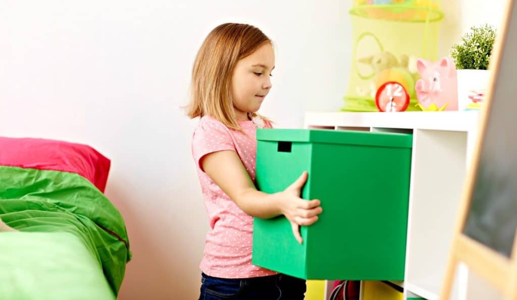 cute little girl putting green box of toys away after her mom used positive reinforcement to change behavior
