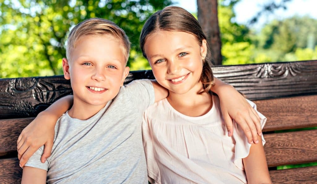 two siblings on park bench hugging after resolving sibling conflict